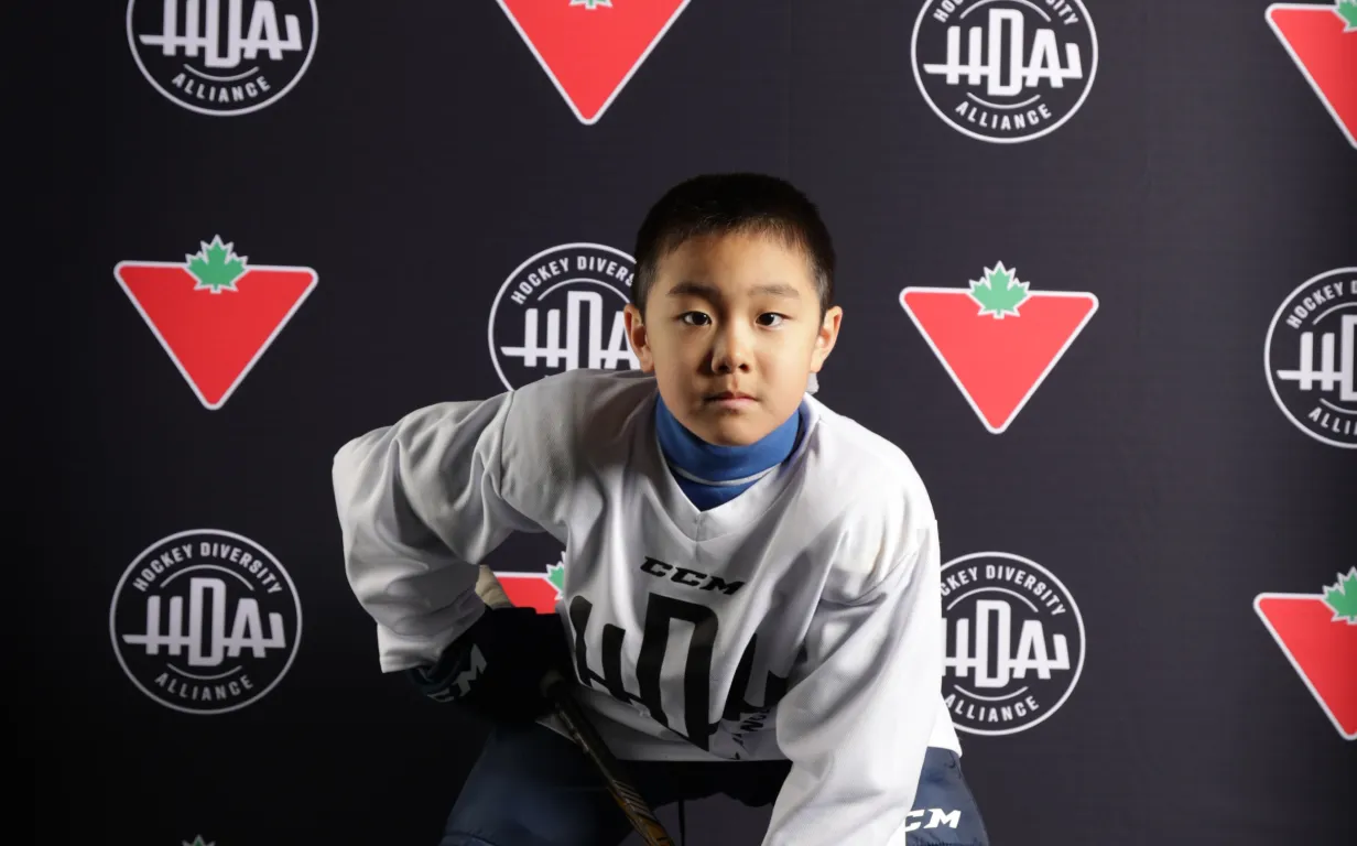 Young hockey player proudly posing in front of the Canadian Tire logo, showcasing passion for the game and community support.